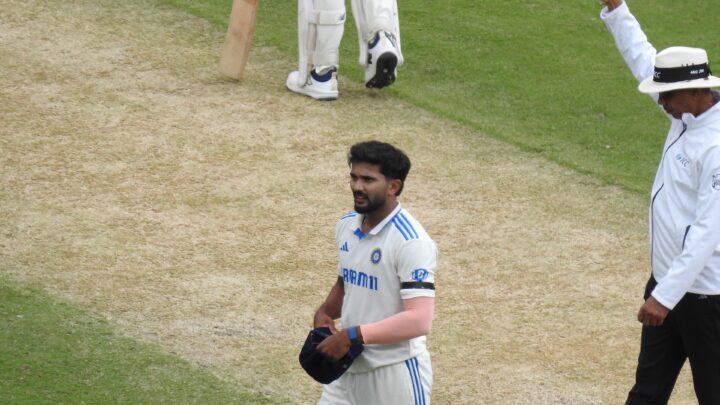 Nitish Kumar Reddy in India's white Test kit walks across the pitch holding his cap, with an umpire signalling beside him.