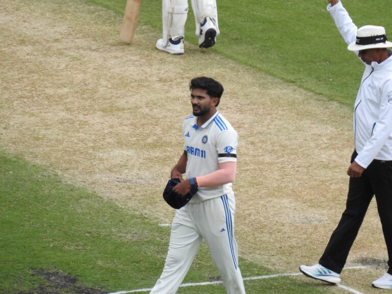 Nitish Kumar Reddy in India's white Test kit walks across the pitch holding his cap, with an umpire signalling beside him.