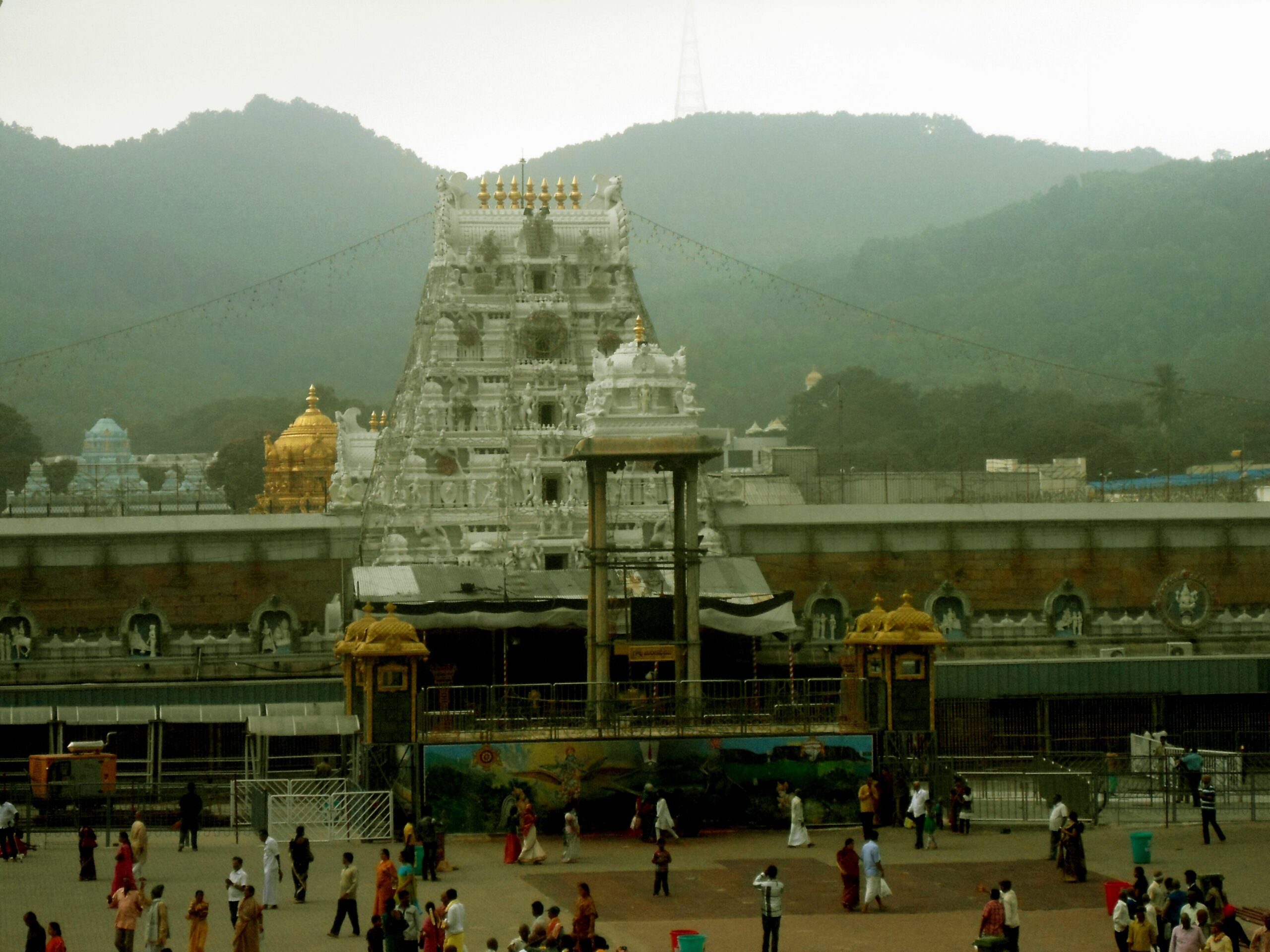 The white main gateway tower of the Tirumala Venkateswara temple, with a golden dome to its left, green hills behind and pilgrims crossing the forecourt (file photo)