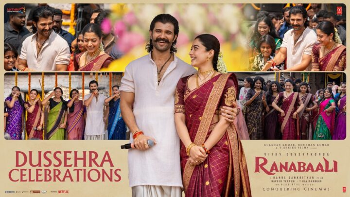 Vijay Deverakonda in a white kurta, holding a microphone, smiles beside Rashmika Mandanna in a maroon silk saree, who looks up at him, on a poster titled Dussehra Celebrations, with smaller photos of the pair among villagers and women in saris behind them.