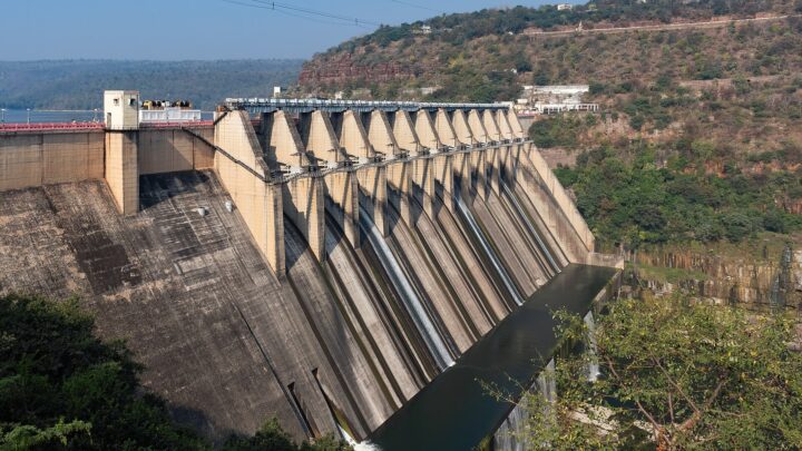 Concrete spillway gates and buttresses of Srisailam dam with water streaming down two channels, hills behind