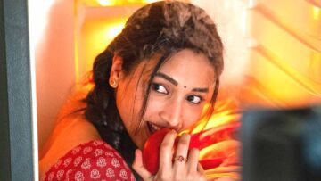 Srinidhi Shetty as Swarna in Aadarsha Kutumbam, biting an apple at an open fridge