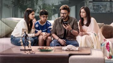Venkatesh sits on a sofa with his on-screen family, looking at a mobile phone.