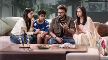Venkatesh sits on a sofa with his on-screen family, looking at a mobile phone.