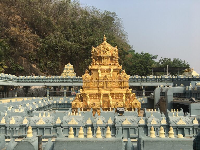 Gold-plated tower of the Kanaka Durga temple with temple walls and a wooded hillside behind it