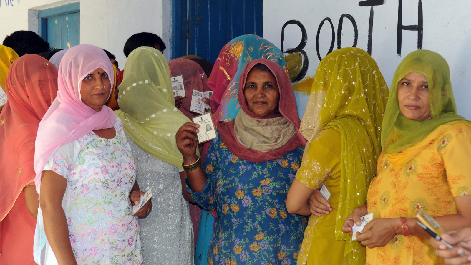 Rural women in colourful dupattas hold up voter ID cards in a queue outside a polling booth