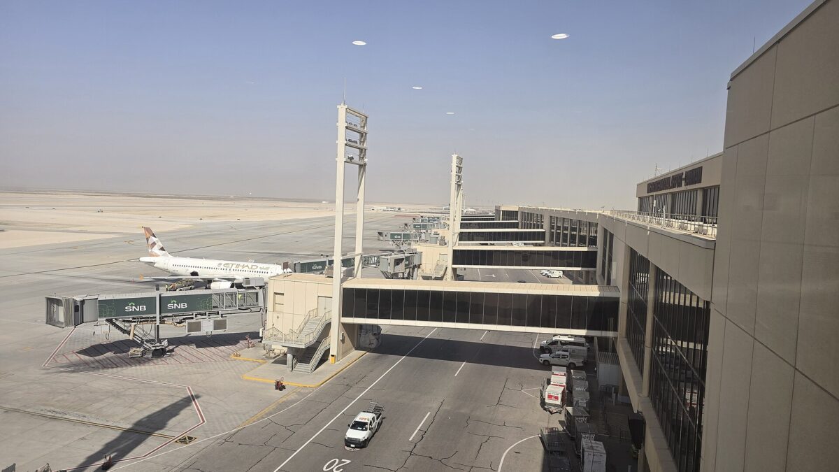 Passenger terminal building and an aircraft at a boarding gate on a sunny day at Dammam airport.
