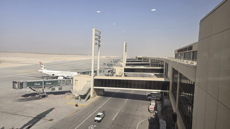 Passenger terminal building and an aircraft at a boarding gate on a sunny day at Dammam airport.