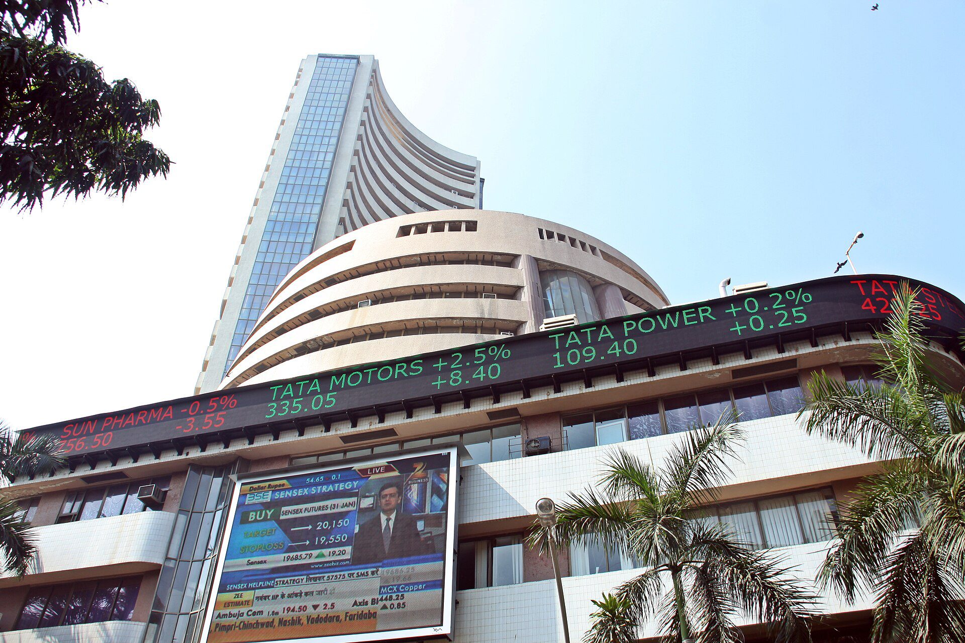 The curved BSE tower and the electronic share-price ticker on its Dalal Street building in Mumbai, seen from street level.