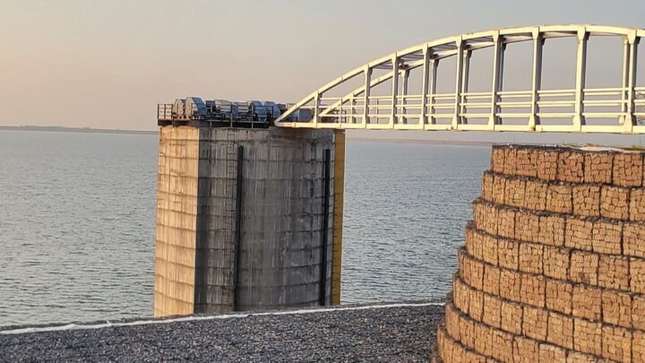A concrete intake tower and an arched white footbridge at the edge of a wide reservoir.