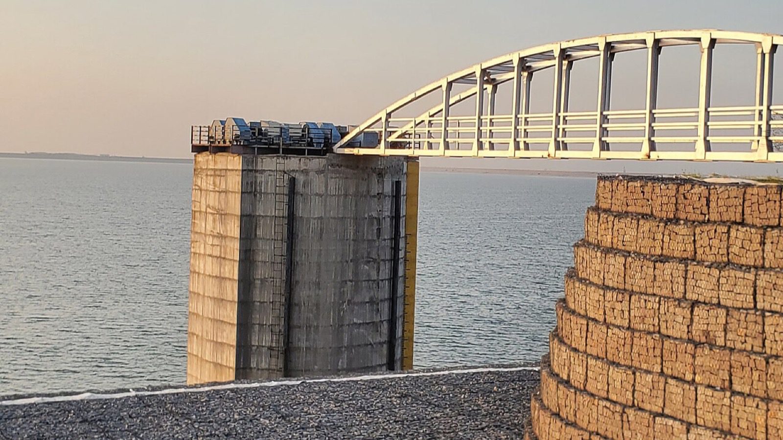 A concrete intake tower and an arched white footbridge at the edge of a wide reservoir.
