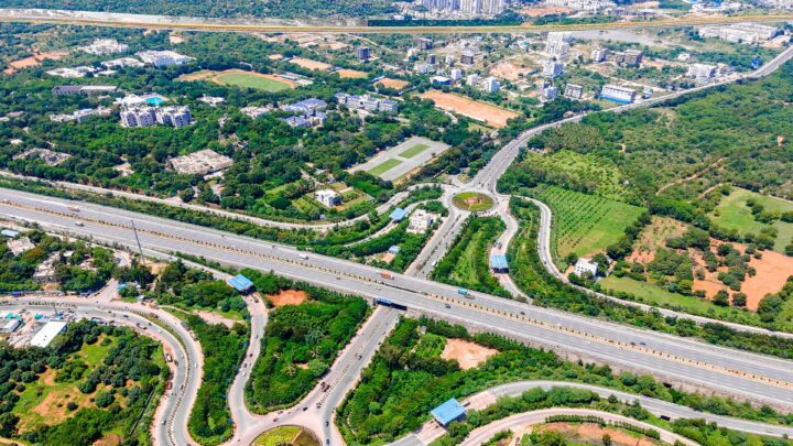 Aerial view of a toll interchange and roundabout on a multi-lane expressway surrounded by greenery