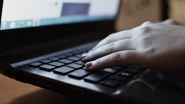A hand resting on the keyboard of a laptop with its screen lit.