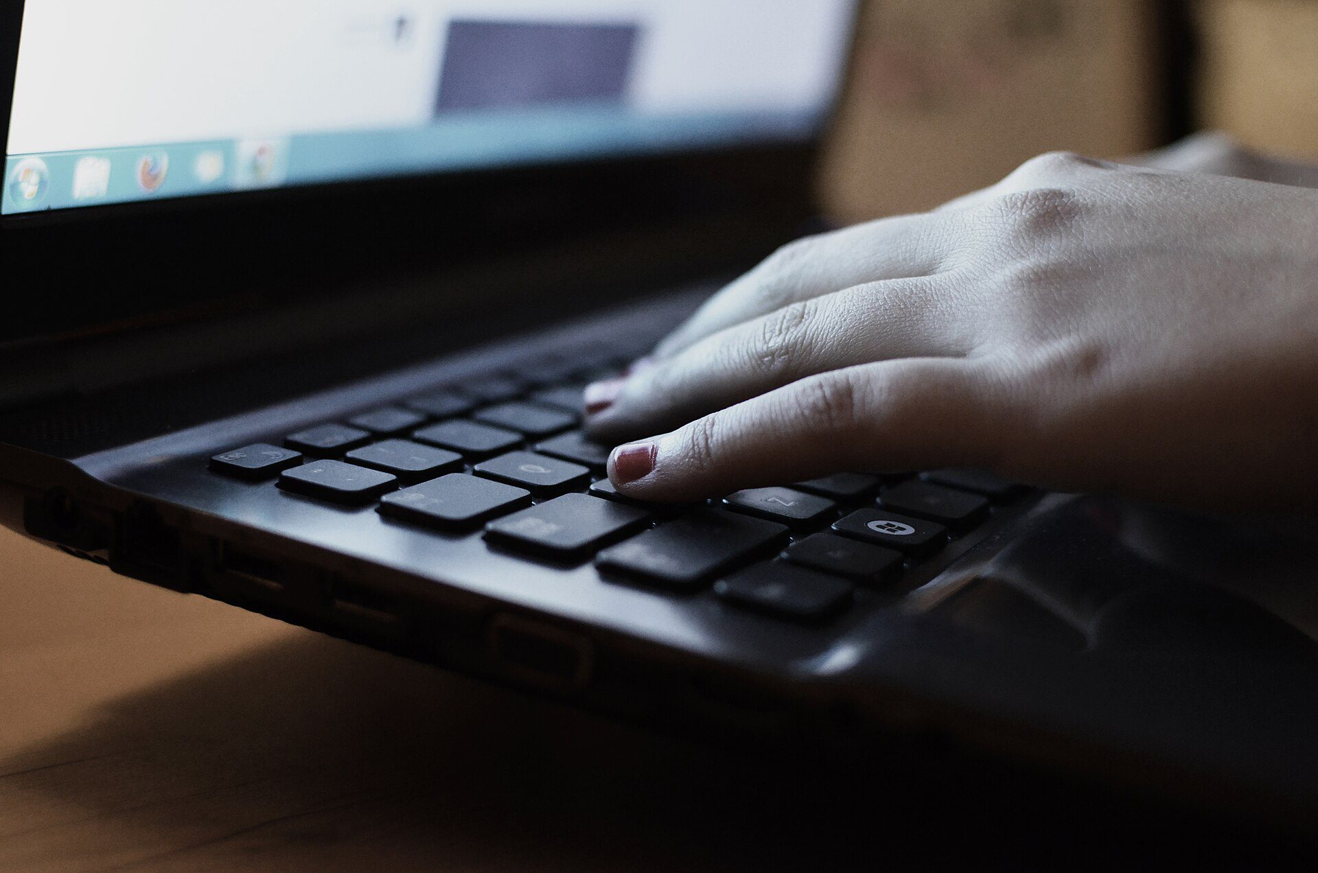 A hand resting on the keyboard of a laptop with its screen lit.
