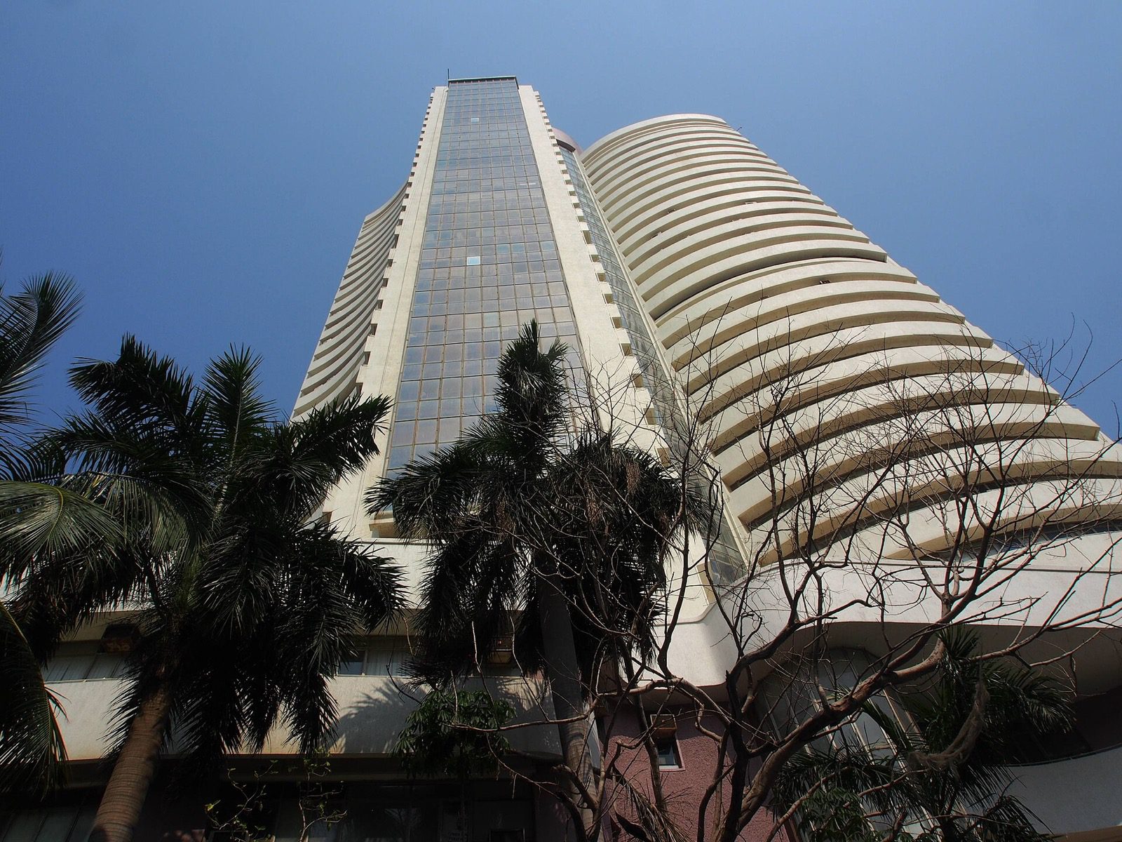The Bombay Stock Exchange tower in Mumbai, seen from below behind palm trees.