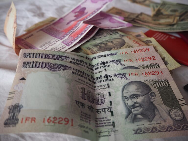 Indian rupee notes of different denominations, with US dollar bills in the background.