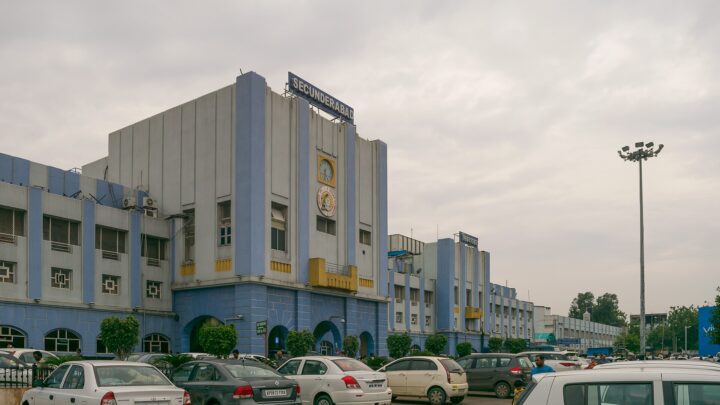 The front of Secunderabad railway station, with cars parked outside under a cloudy sky.