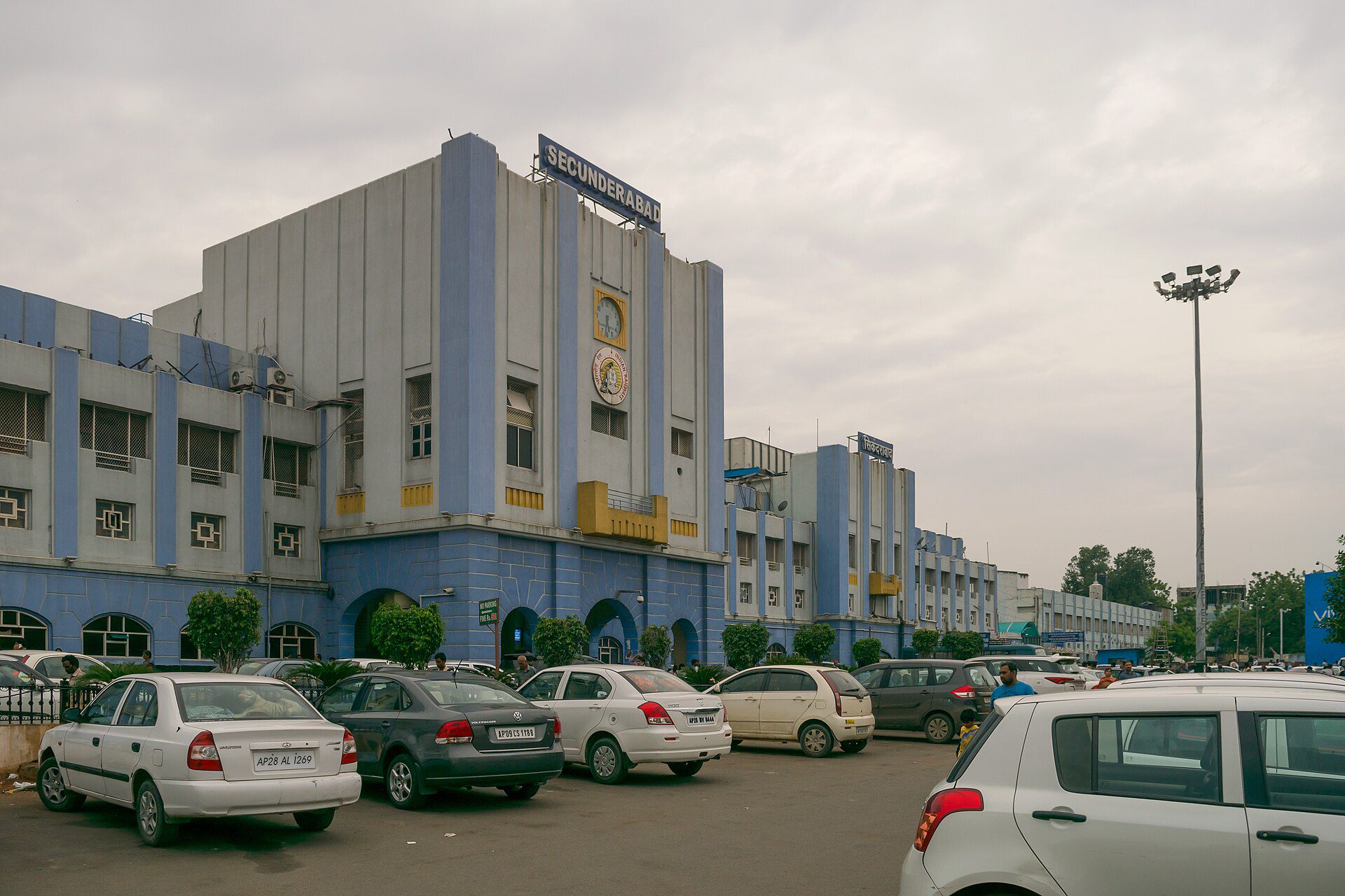The front of Secunderabad railway station, with cars parked outside under a cloudy sky.